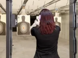 A woman taking aim on a paper target in an indoor firing range.