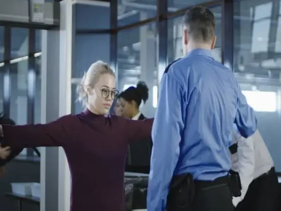 A woman with her arms outstretched as a security officer scans her at an airport security check point.