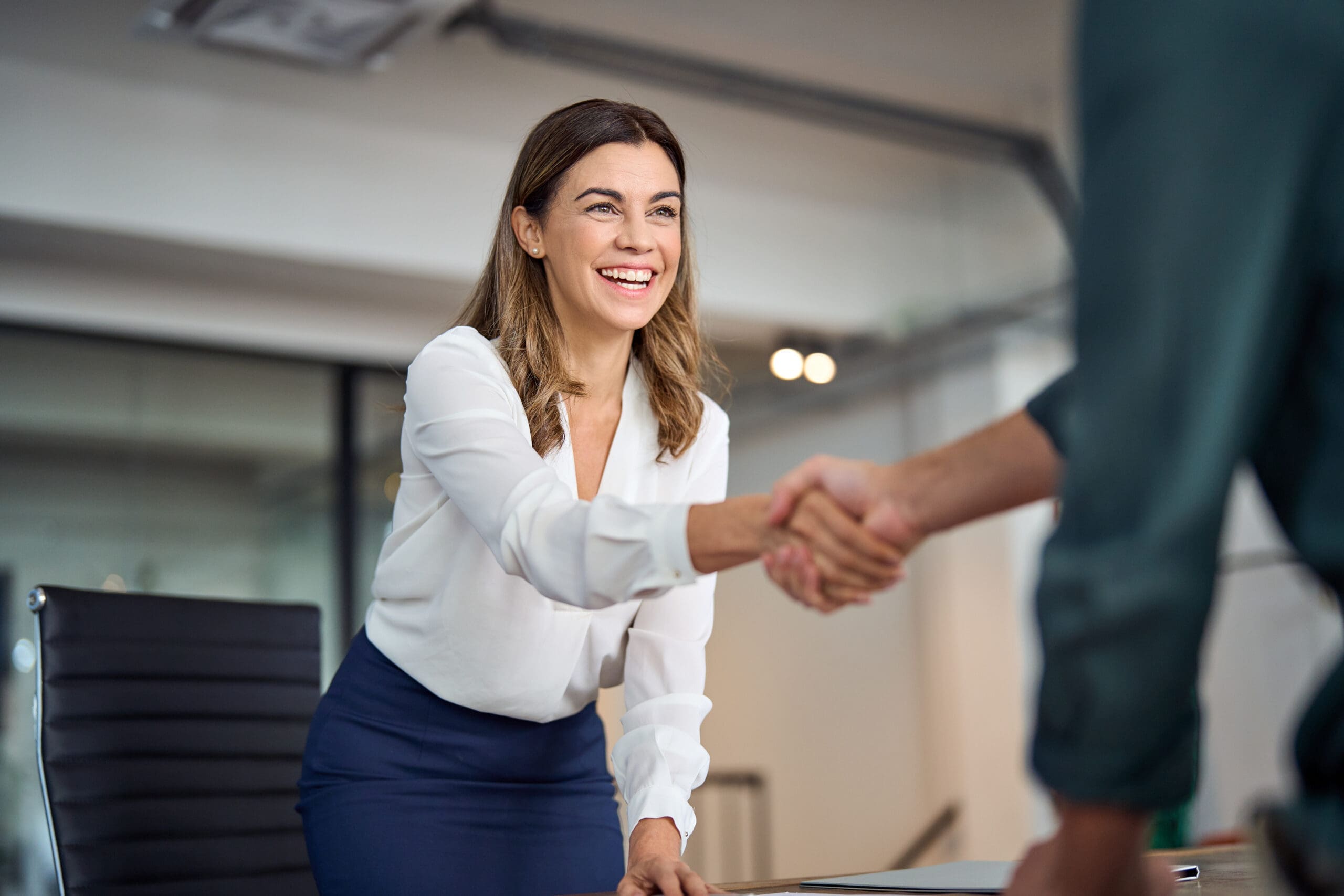 Happy mid aged business woman manager handshaking greeting client in office. Happy mid aged business woman manager handshaking greeting client in office.